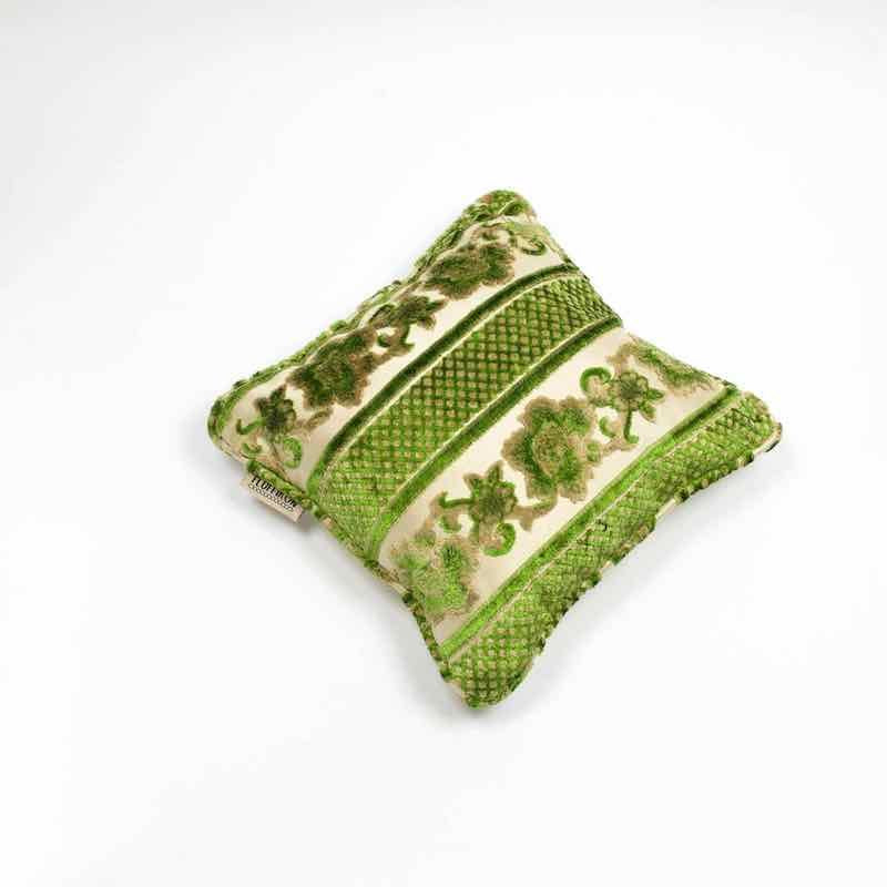 Green moroccan velvet cushion in front of white background.