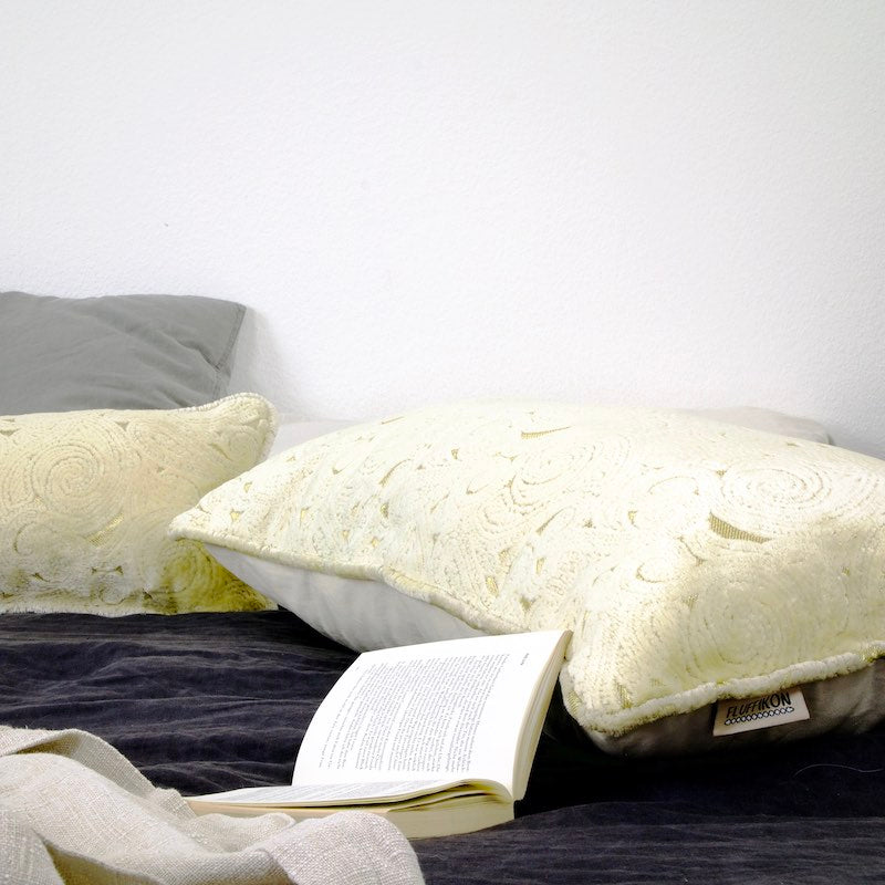Two large beige Fluffikon pillows laying on a bed. An open book is laying in front of one pillow.