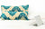 Two beige/turquoise large Moroccan throw pillows on a white bed. A laptop is standing on the bed.