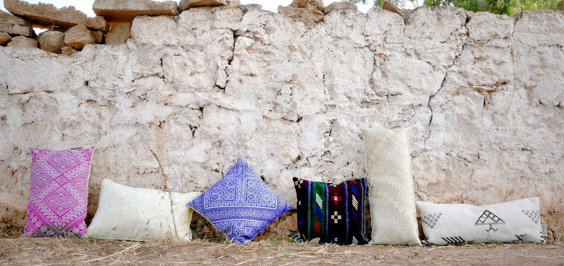Six decorative Moroccan pillows in front of stone wall