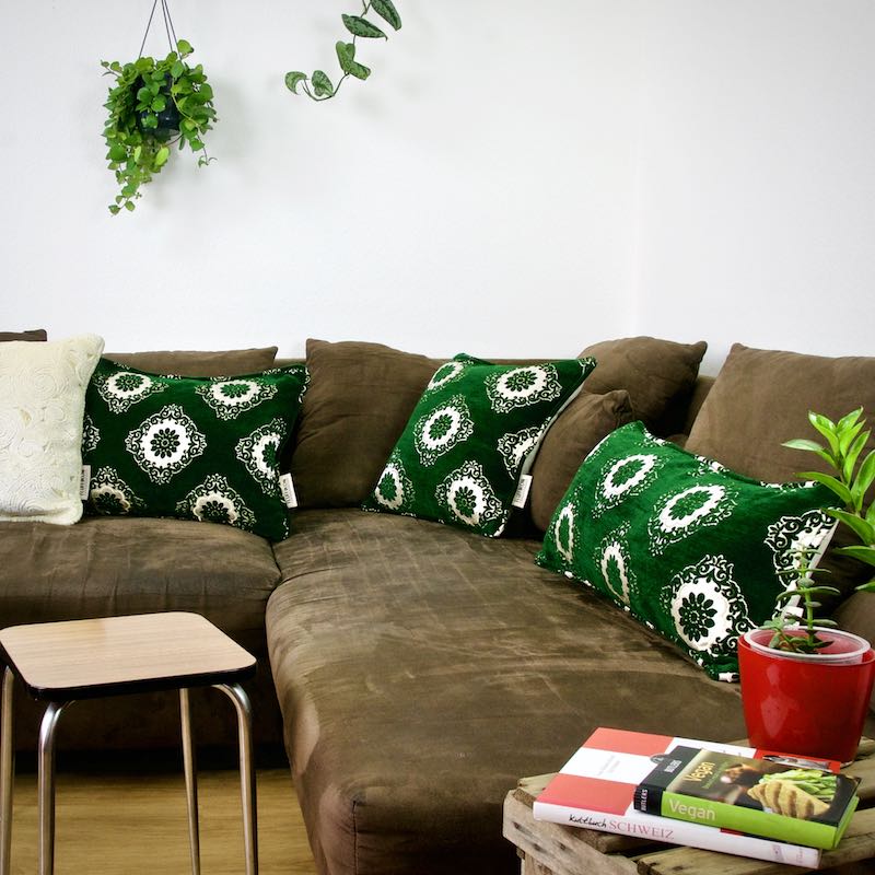 Three green velvet throw pillows on a brown couch. The pillows have traditional Moroccan tile patterns.