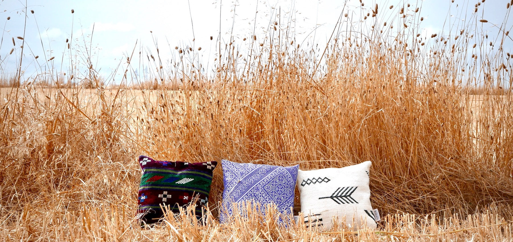 Three square pillows with traditional Moroccan patterns on a hay field.