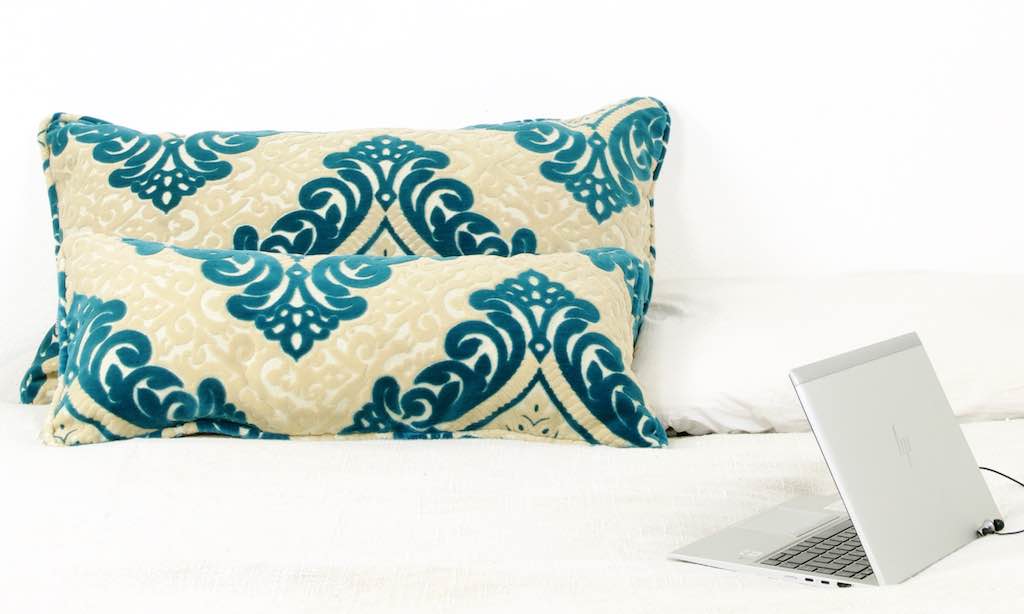 Two turquoise beige colored cushions on a bed.