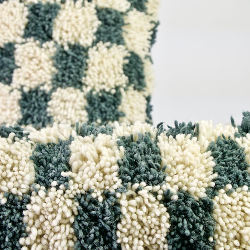 Two Fluffikon checkered Moroccan wool pillows. The pillows are made from a Beni Ourain Moroccan wool rug. The focal point is on the front pillow. The pillow in the background is out-of-focus.
