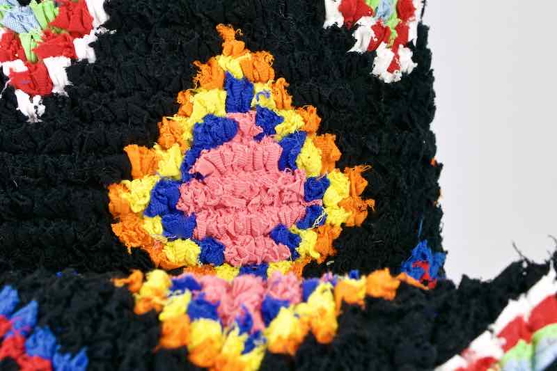 Zoom on a black Flufikon Boucherouite throw pillow. The pillow has red and yellow Moroccan pattern.