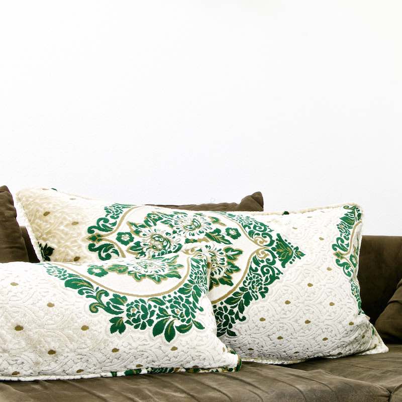 Zwei grün, beige, braune orientalische Marokko Kissen auf einer brauen Couch mit typischen marokkanischen Motiven.