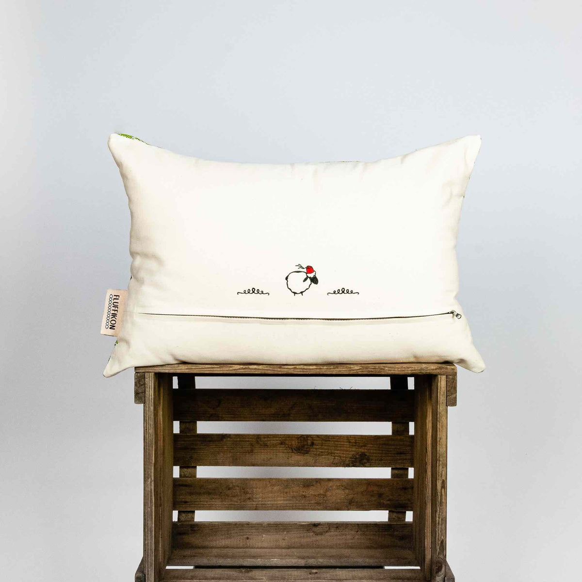 Fluffikon silk rectangular pillow made from green moroccan fabric. The pillow is shown from the back on a wooden box. Size 40x60 cm.