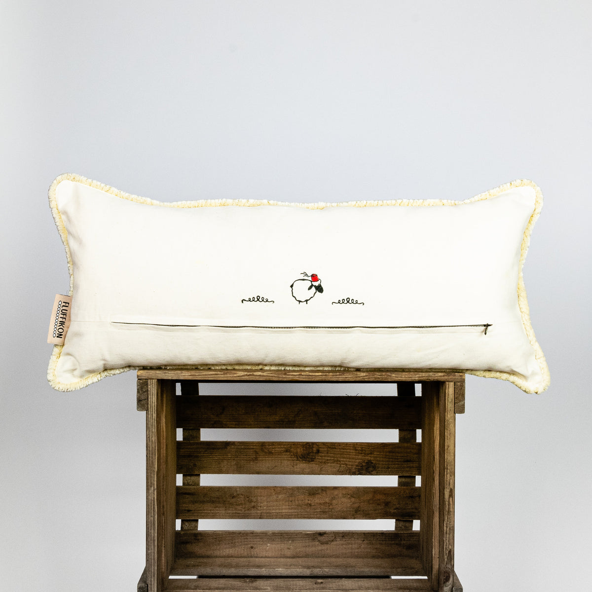 Fluffikon velvet lumbar pillow made from beige moroccan fabric. The pillow is on a wooden box. The pillow back is shown.