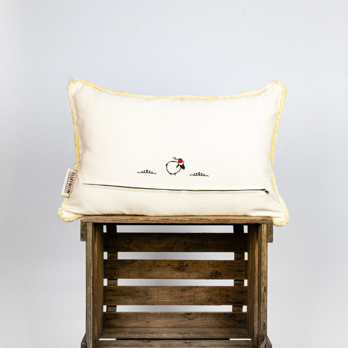 Fluffikon velvet rectangular pillow made from beige moroccan fabric. The pillow is on a wooden box. The pillow back is shown.