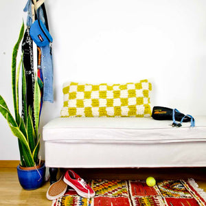Beni Ourain Fluffikon lumbar pillow with yellow white checkered pattern made from a wool carpet. The pillow is standing on a white bench.