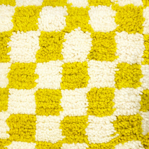 Zoom on a Beni Ourain Fluffikon pillow with yellow white checkered pattern. The pillow is made from wool. The structure of the wool is visible with many details.
