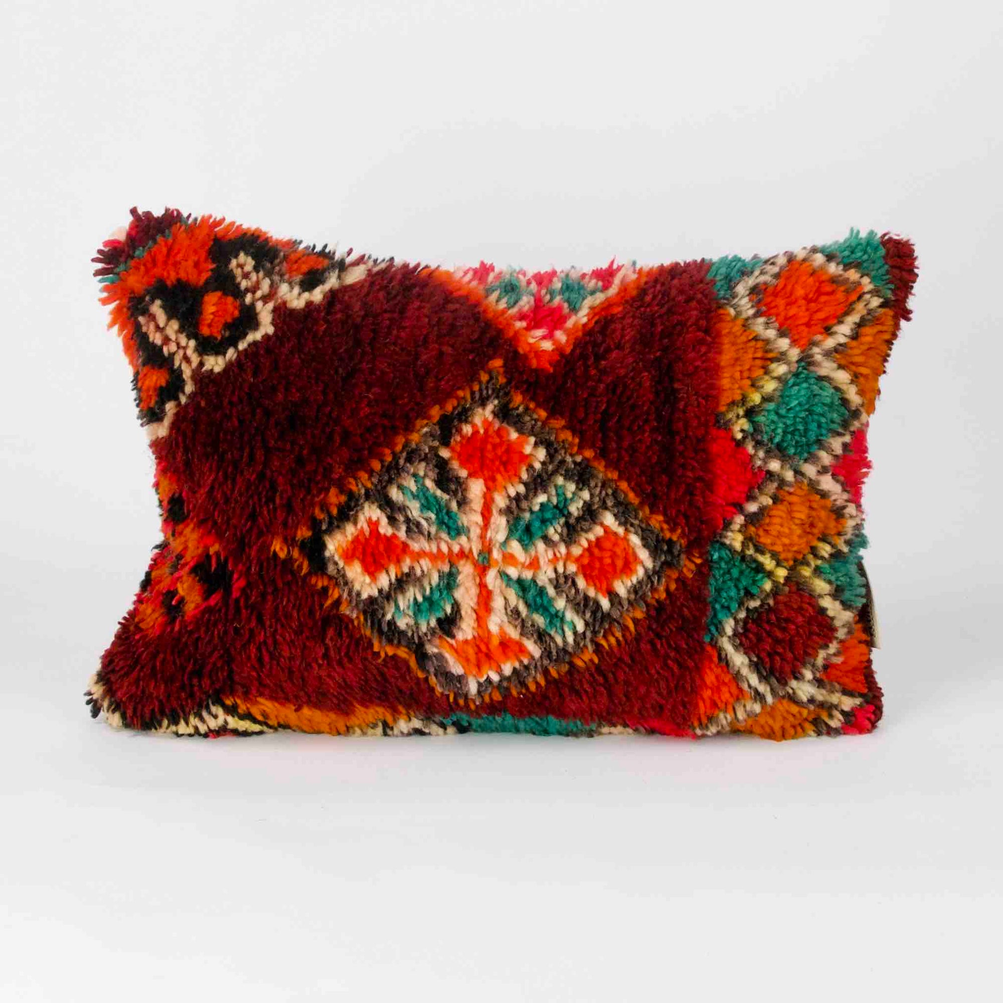 A red rectangular Berber cushion made from a vintage rug is standing in front of a white background.