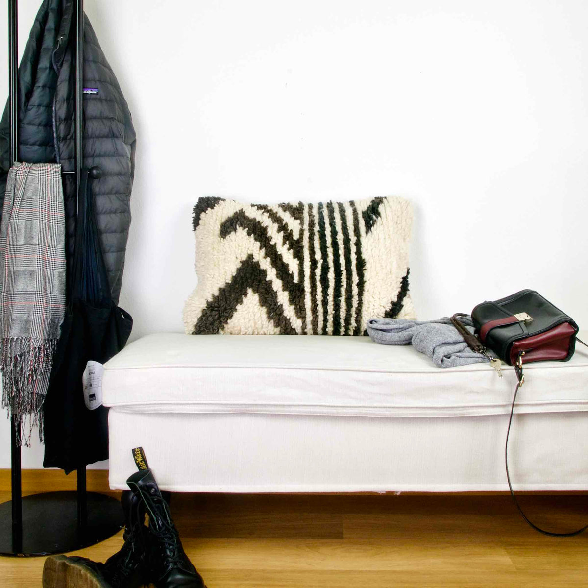 Black and white Fluffikon rug pillow on a white bench. A leather bag is laying on the bench.