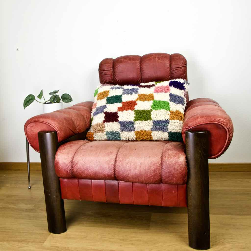 Colorful checkered  Fluffikon throw Pillow on a red leather chair