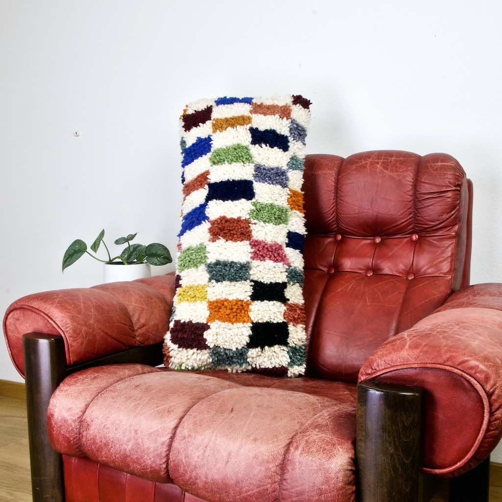 Colorful lumbar Fluffikon pillow on a red leather chair.