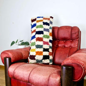 Colorful lumbar Fluffikon pillow on a red leather chair.