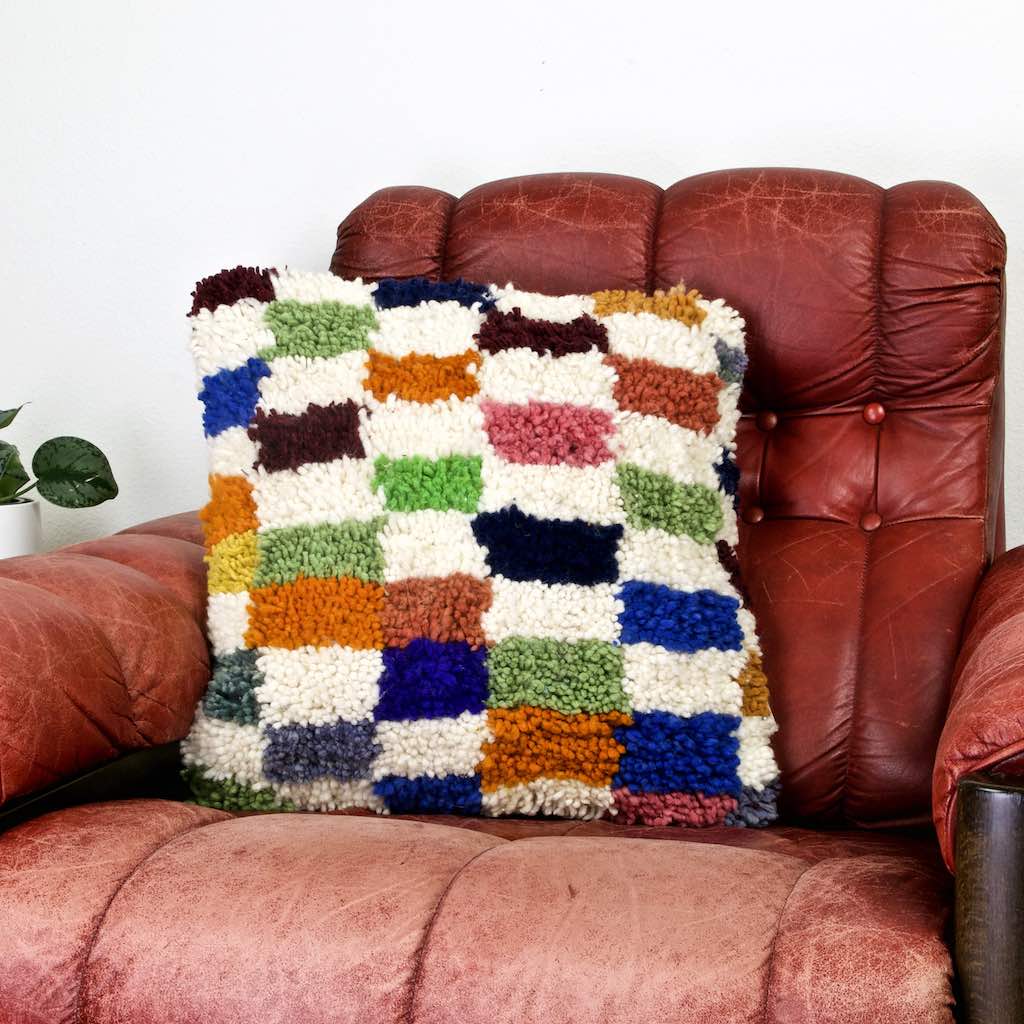 Colorful checkered Fluffikon throw pillow on a red leather chair.