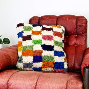 Colorful checkered Fluffikon throw pillow on a red leather chair.