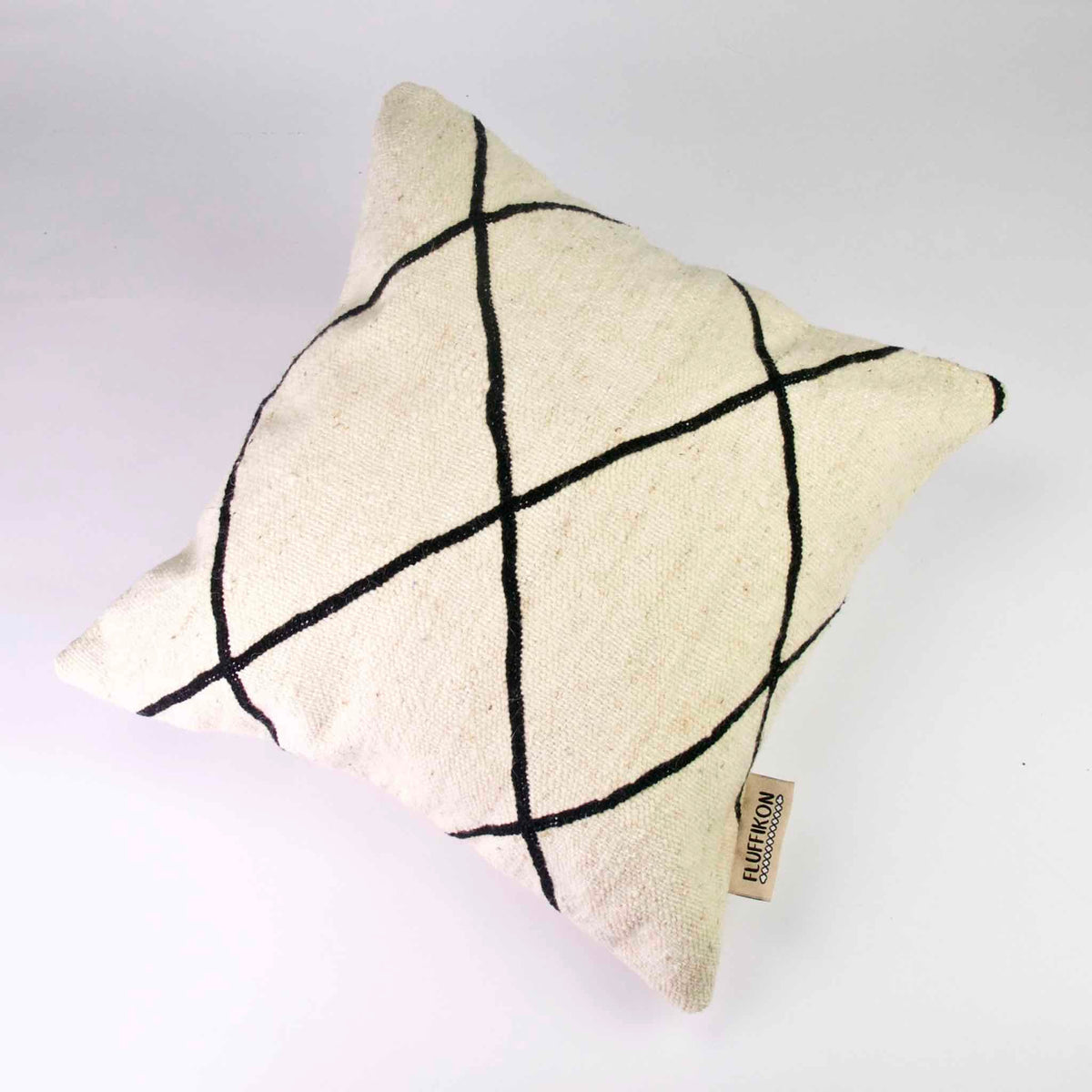 Square Fluffikon Kilim pillow cover on the ground. The pillows is made from a black and white Kilim rug.
