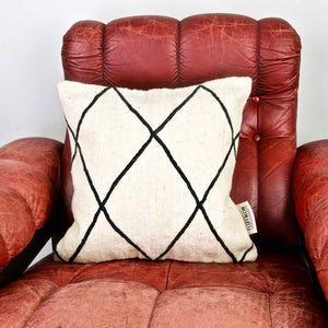 Zoom on square Fluffikon Kilim pillow cover on a red leather chair.
