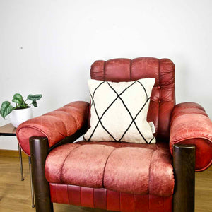 Square Fluffikon Kilim pillow cover on a red leather chair.