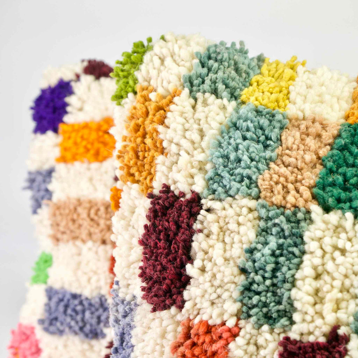 Zoom auf die Ecke eines Fluffikon Kinderzimmer Kissens. Ein weiteres Kissen ist verschwommen im Hintergrund. Das Kissen ist bunt kariert.