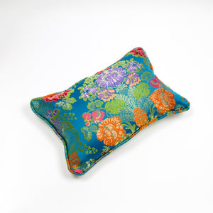 Blue Fluffikon decorative rectangular pillow made from shiny brocade with colourful flowers embroidery. The front of the pillow is shown. Pillow is on the ground.