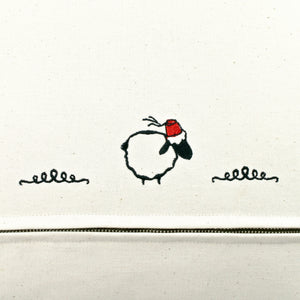 Detailed view on the beige cotton fabric of the back of a Fluffikon pillow. A stitched sheep with a red traditional moroccan hat (Fez) is shown.