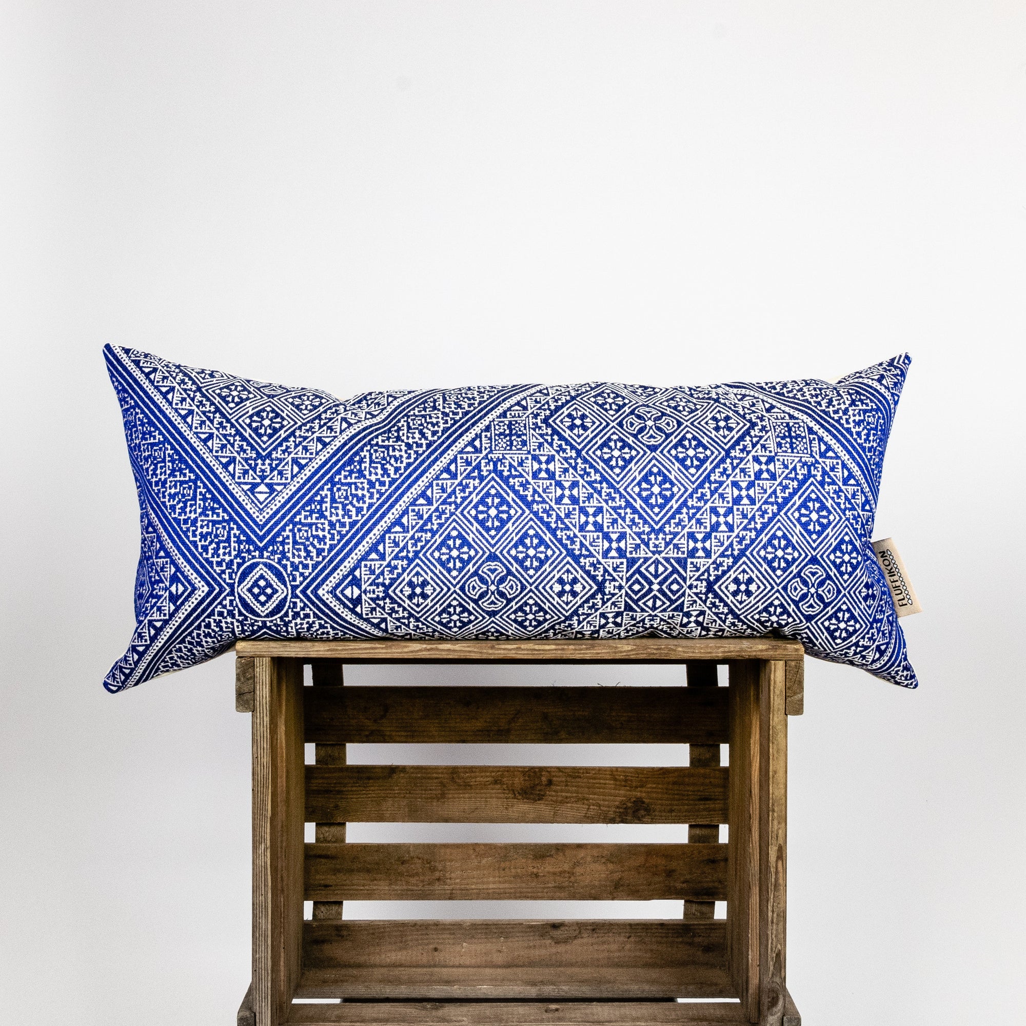 Blue-white decorative lumbar pillow made from silk with moroccan pattern. Pillow on a wooden box.
