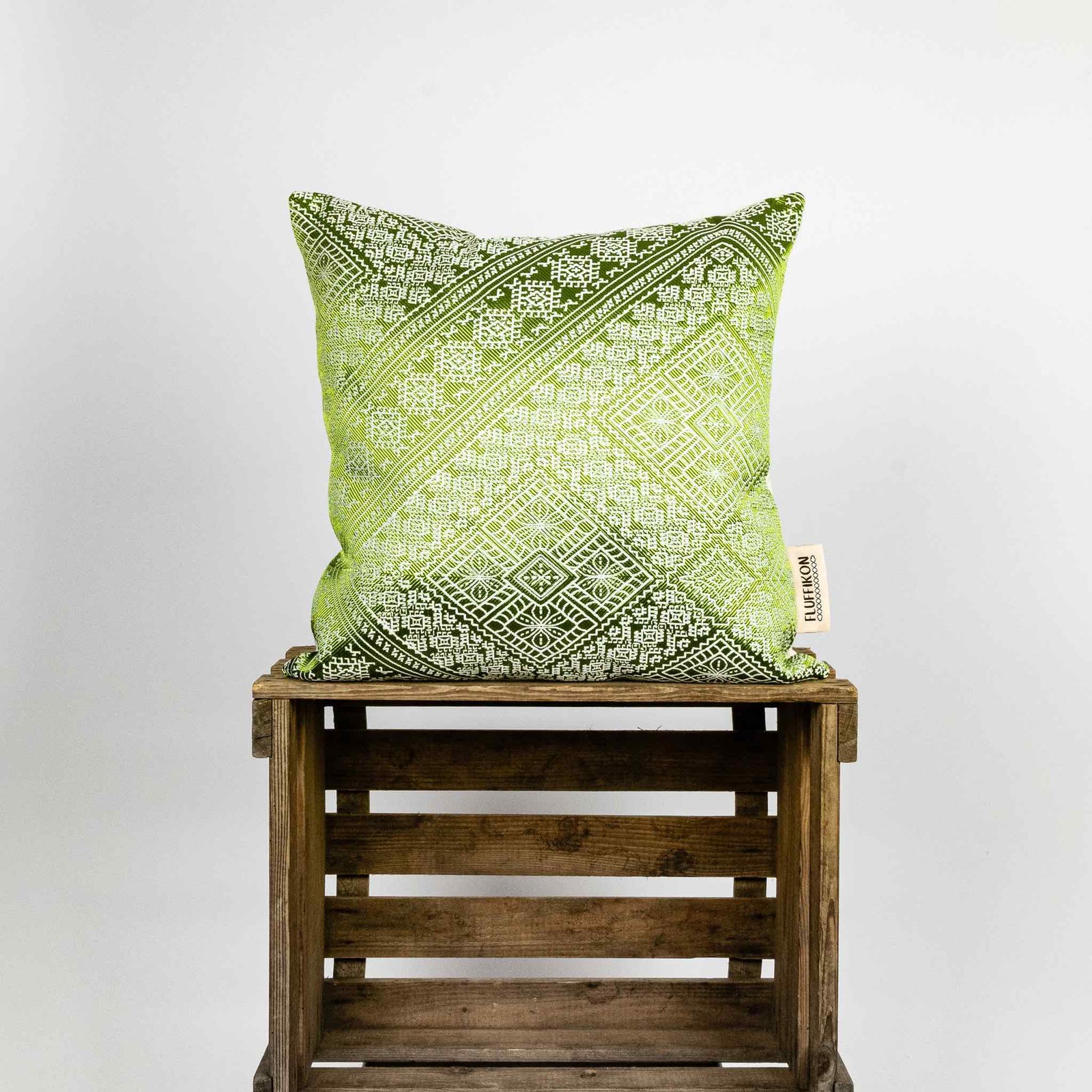 Fluffikon silk square pillow made from green moroccan fabric. The pillow is on a wooden box. Size 45x45 cm.