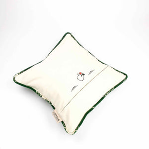 The back of a green velvet throw pillow showing the stitching of sheep with a red hat.