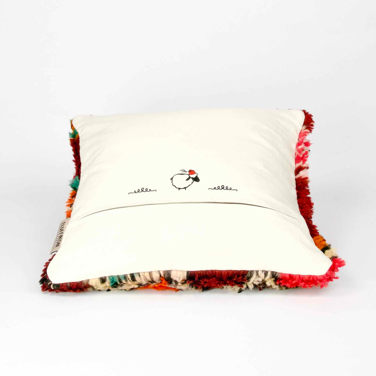 Red Berber pillow made from a vintage wool rug is lying on the ground.