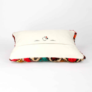 A red rectangular Berber pillow made from a vintage rug is laying in front of a white background.