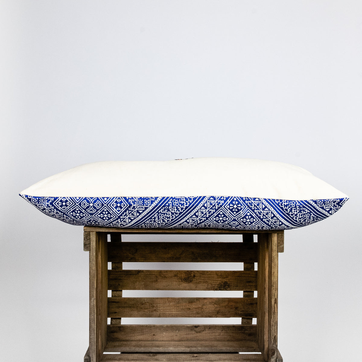 Blue-white decorative lumbar pillow made from silk with moroccan pattern. Pillow shown from the side. Pillow on wooden box.