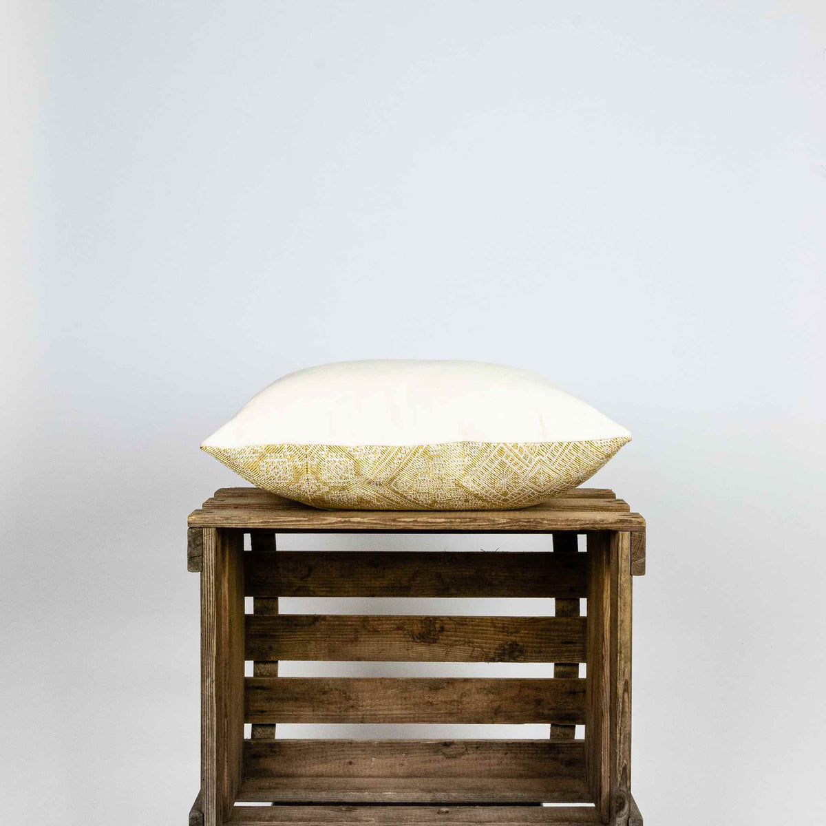 Fluffikon silk square pillow made from golden moroccan fabric. The pillow is on a wooden box shown from the side.