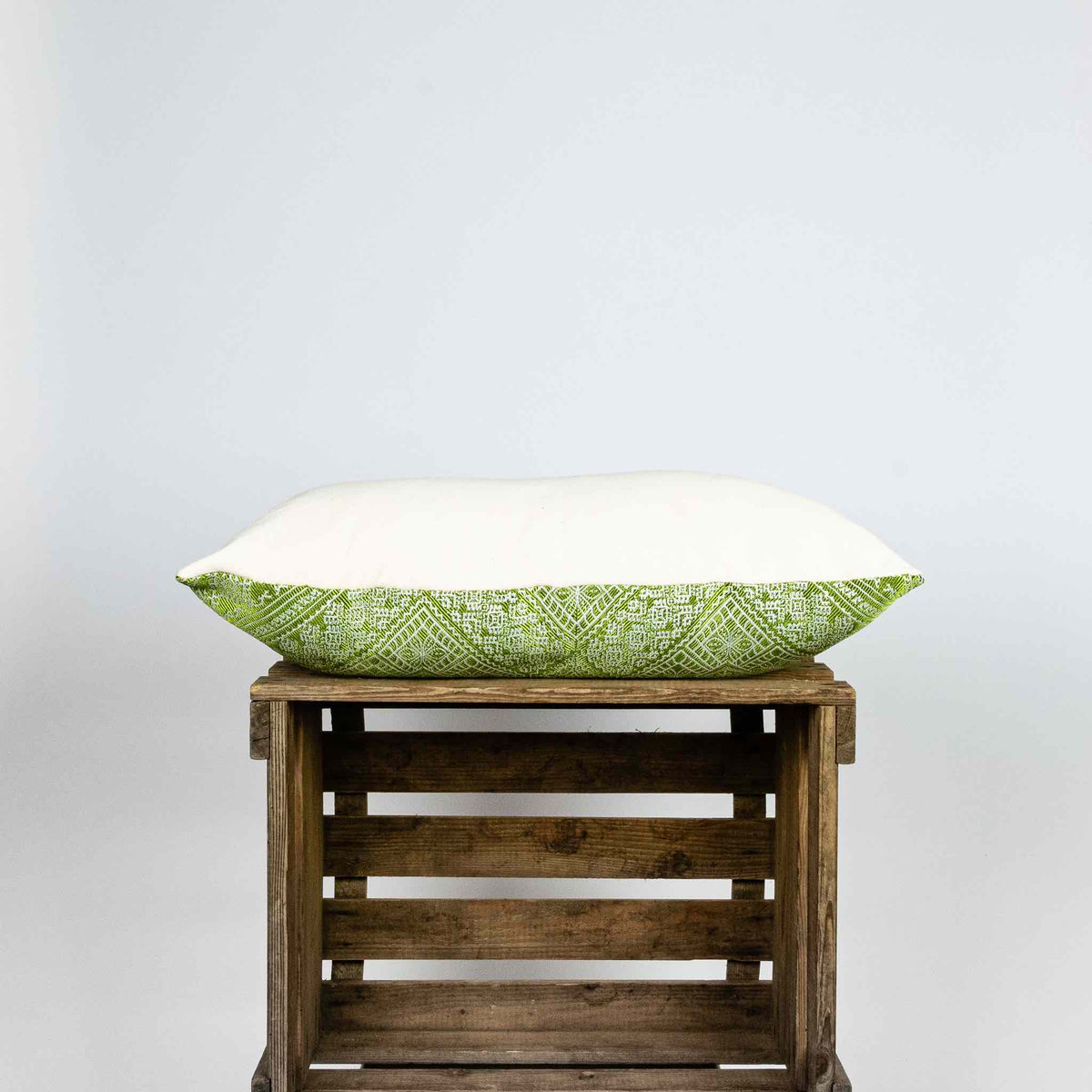 Fluffikon silk rectangular pillow made from green moroccan fabric. The pillow is shown from the side on a wooden box. Size 40x60 cm.