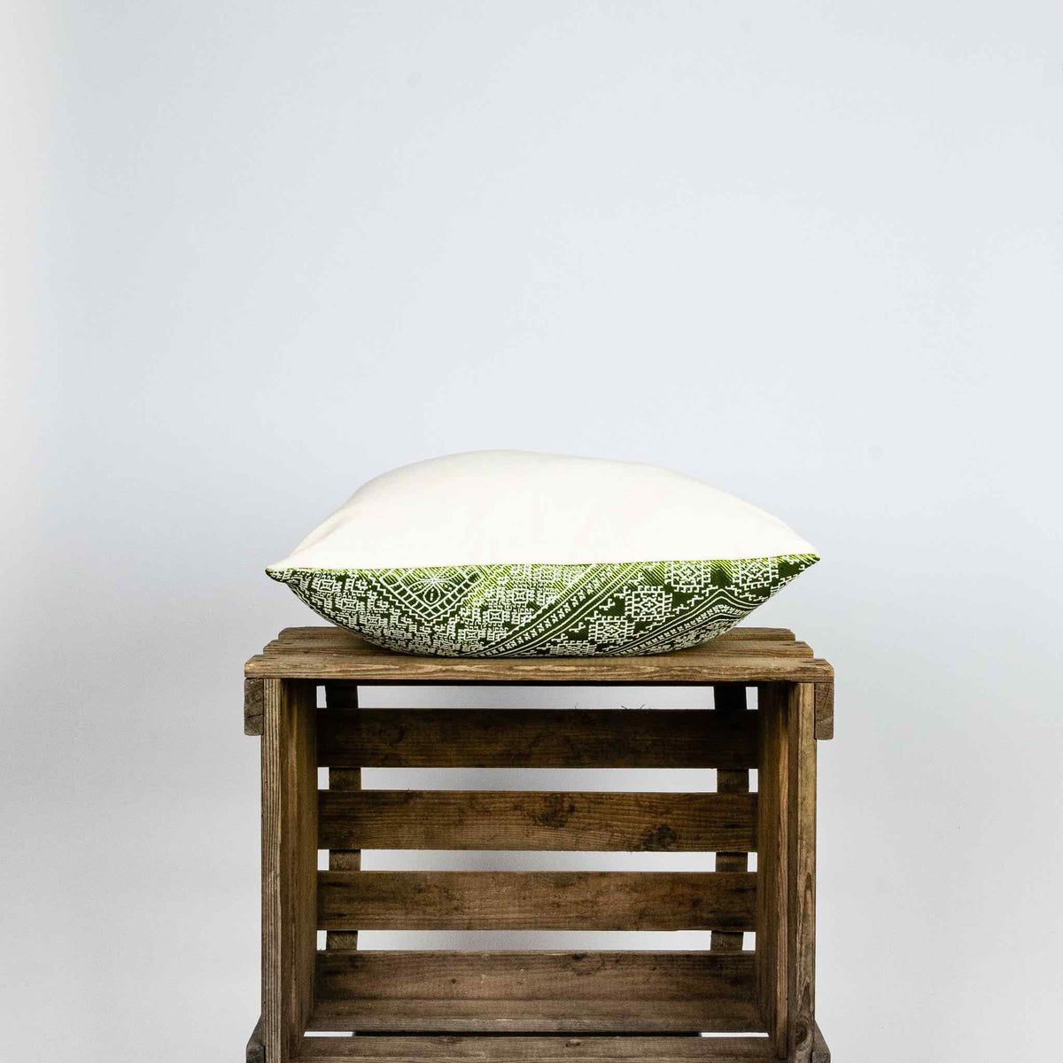 Fluffikon silk square pillow made from green moroccan fabric. The pillow is shown from the side on a wooden box. Size 45x45 cm.