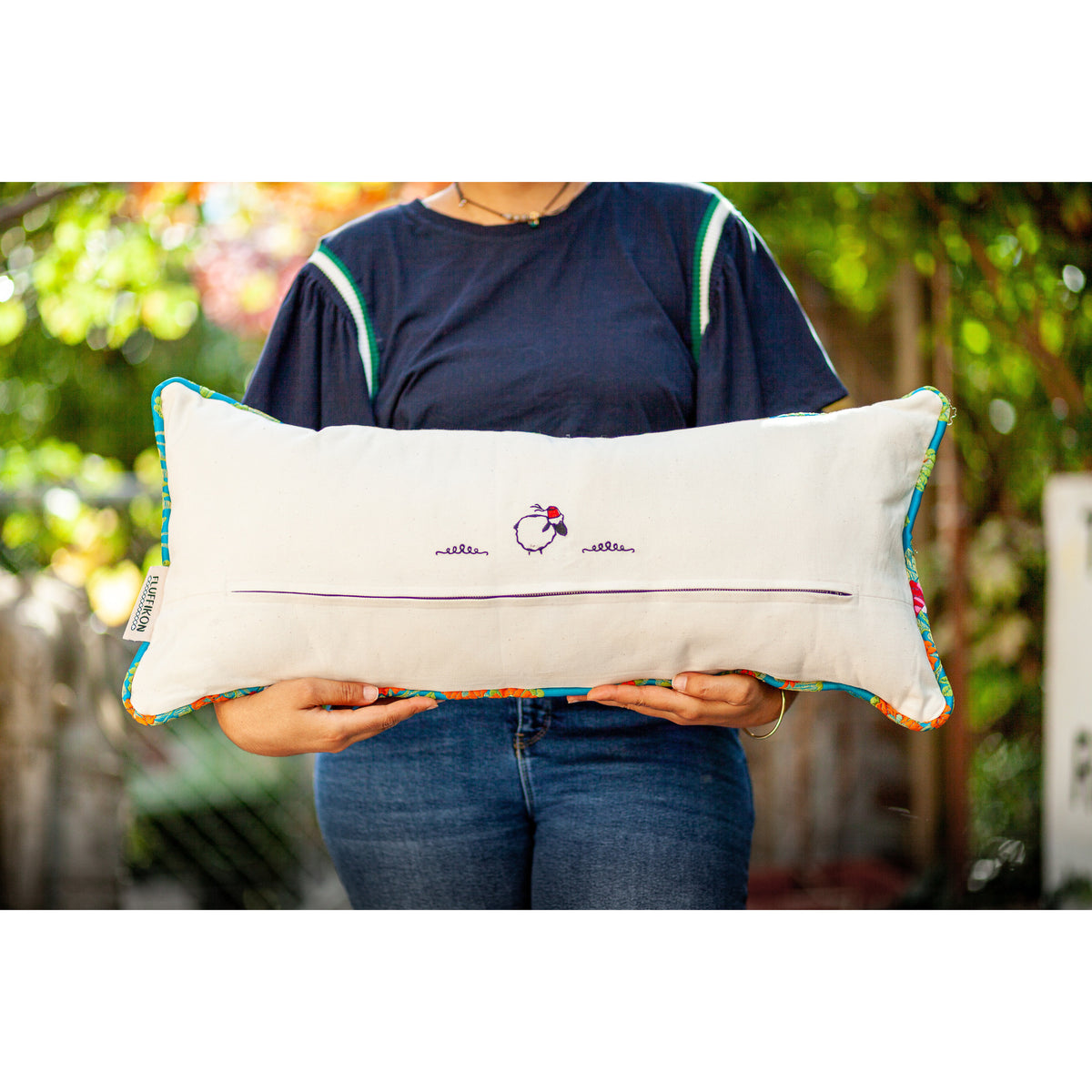 Woman holding a blue decorative lumbar pillow made from shiny brocade with colourful flowers embroidery. Back of the pillow made from white cotton.