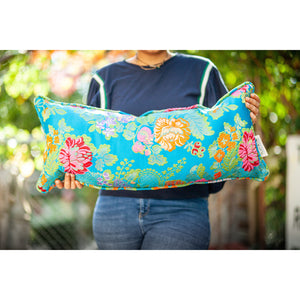 Woman holding blue decorative lumbar pillow made from shiny brocade with colourful flowers embroidery.