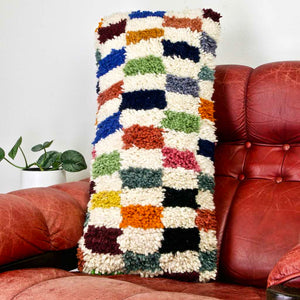 Zoom on a colorful lumbar Fluffikon pillow on a red leather chair.