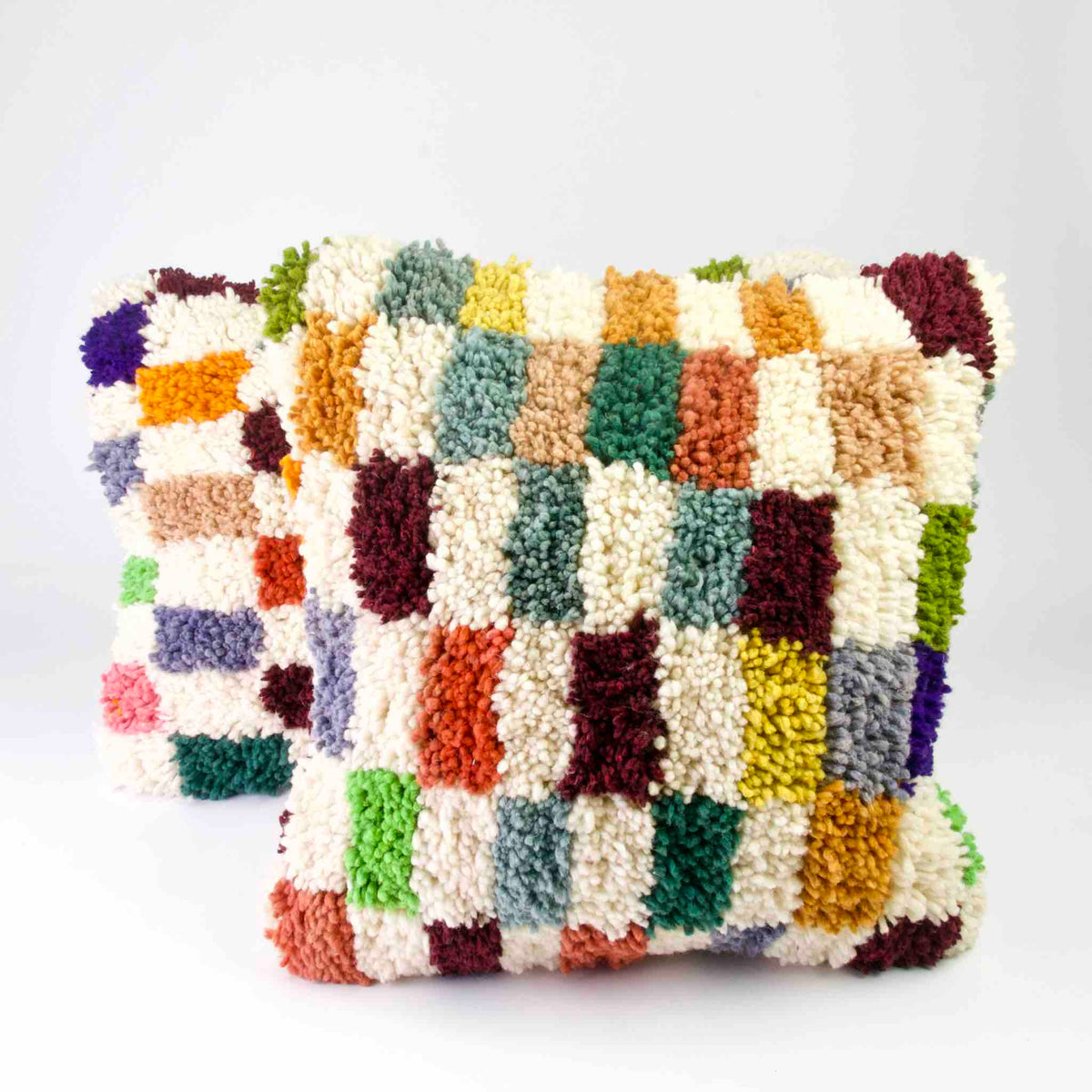 Zwei Fluffikon Kinderzimmer Kissen vor weissem Hintergrund. Die Kissen sind bunt kariert.