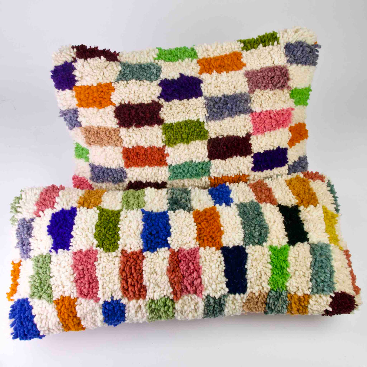 Zwei Fluffikon Kinderzimer Zierkissen vor einem weissen Hintergrund. Die Kissen sind bunt kariert.