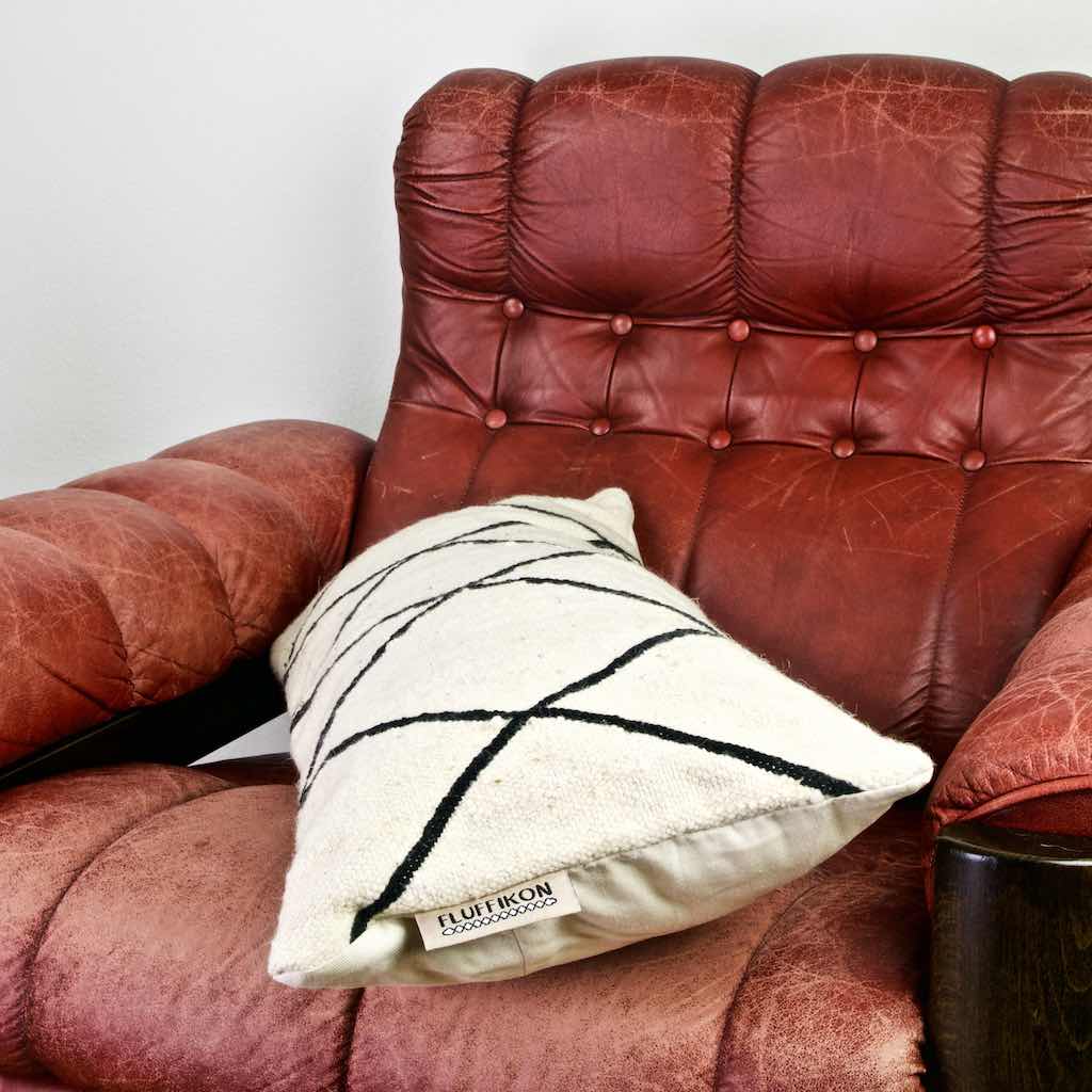 Black and white Fluffikon Kilim pillow on a red leather chair.