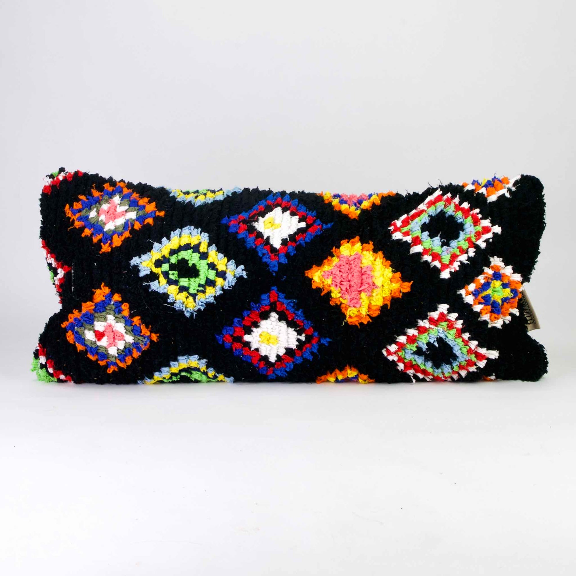 Black Fluffikon Boucherouite lumbar pillow. The Moroccan pillow is made from upcycled clothes. It has colorful patterns in yellow, red, blue and green.