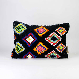 A black Fluffikon Boucherouite throw pillow. The upcycled pillow has colorful patterns embedded in the black fabric.