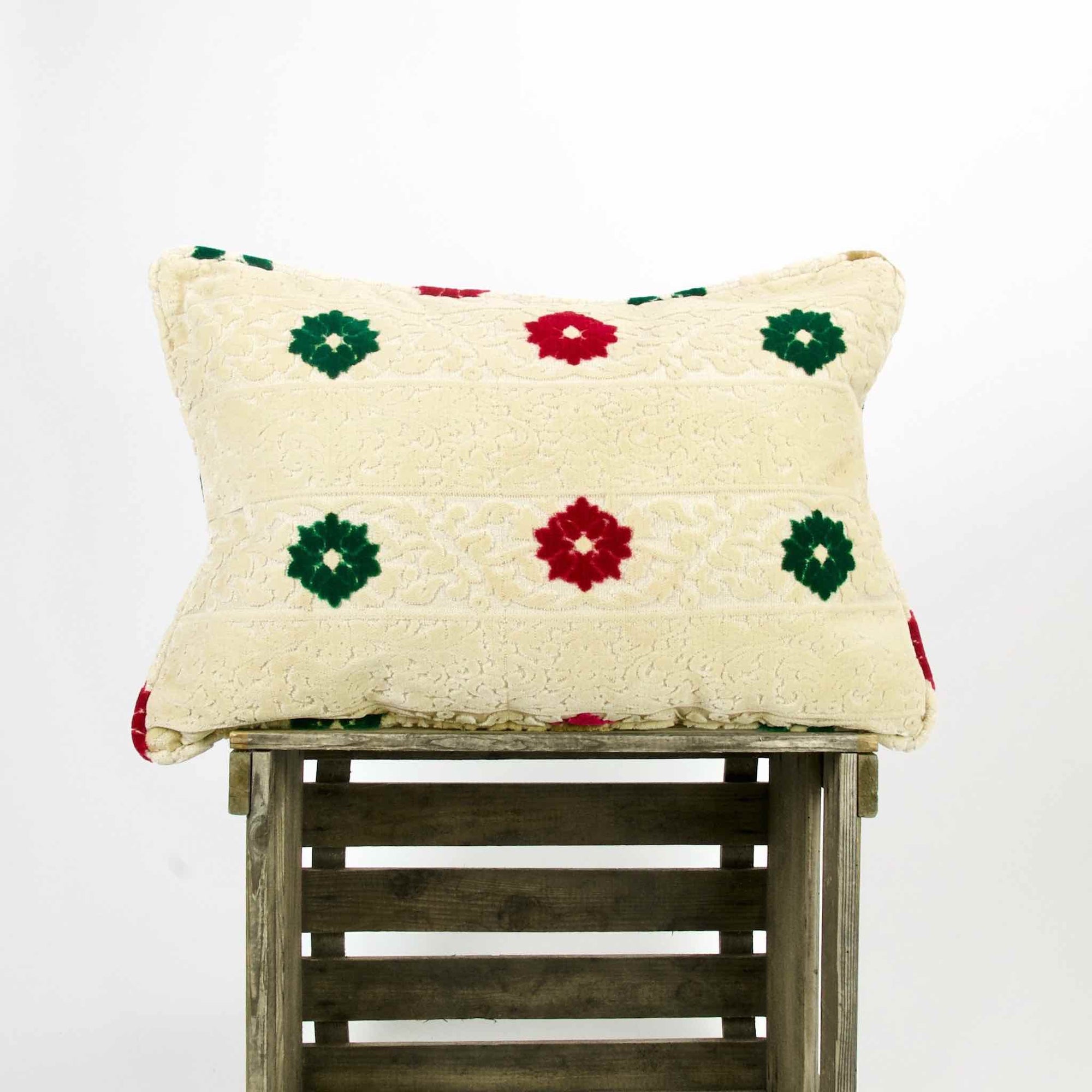 Beige Velvet Fluffikon sofa pillow with red and green flowers on a wooden box.