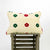 Beige Velvet Fluffikon sofa pillow with red and green flowers on a wooden box.