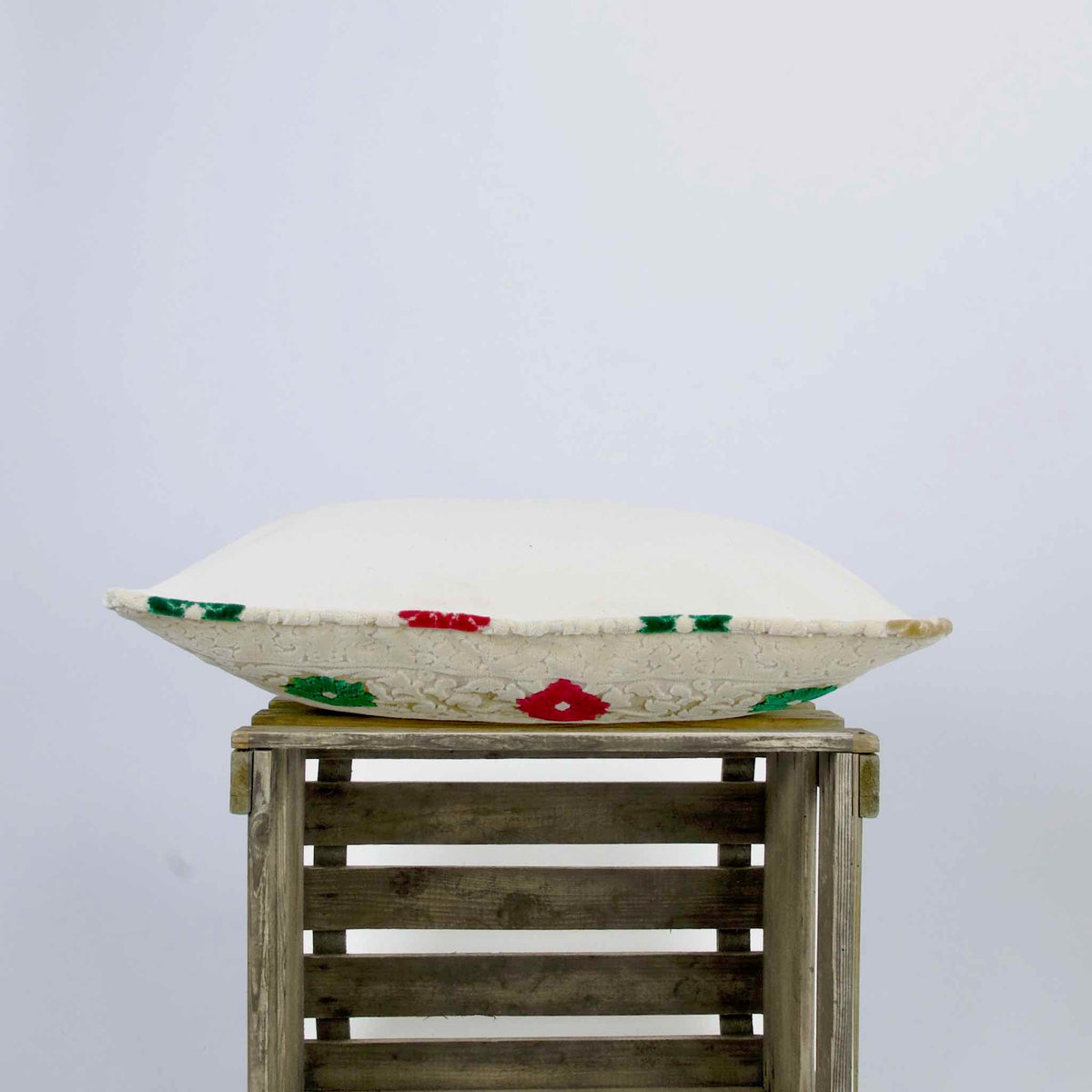 Side view on a sofa pillow made from Moroccan velvet. The pillow is lying on a wooden box.