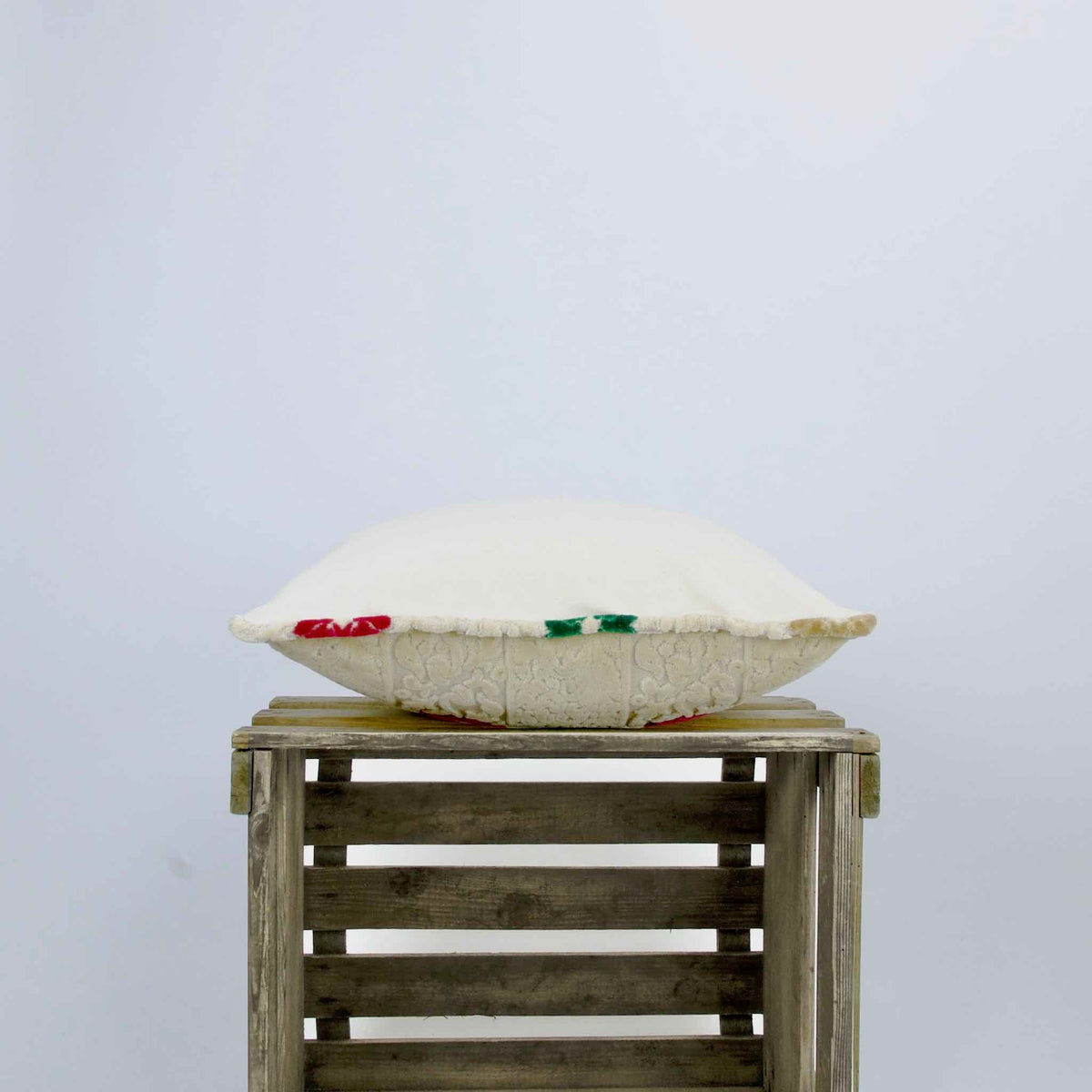 Side view of a velvet square pillow. The pillows is placed on a wooden box.