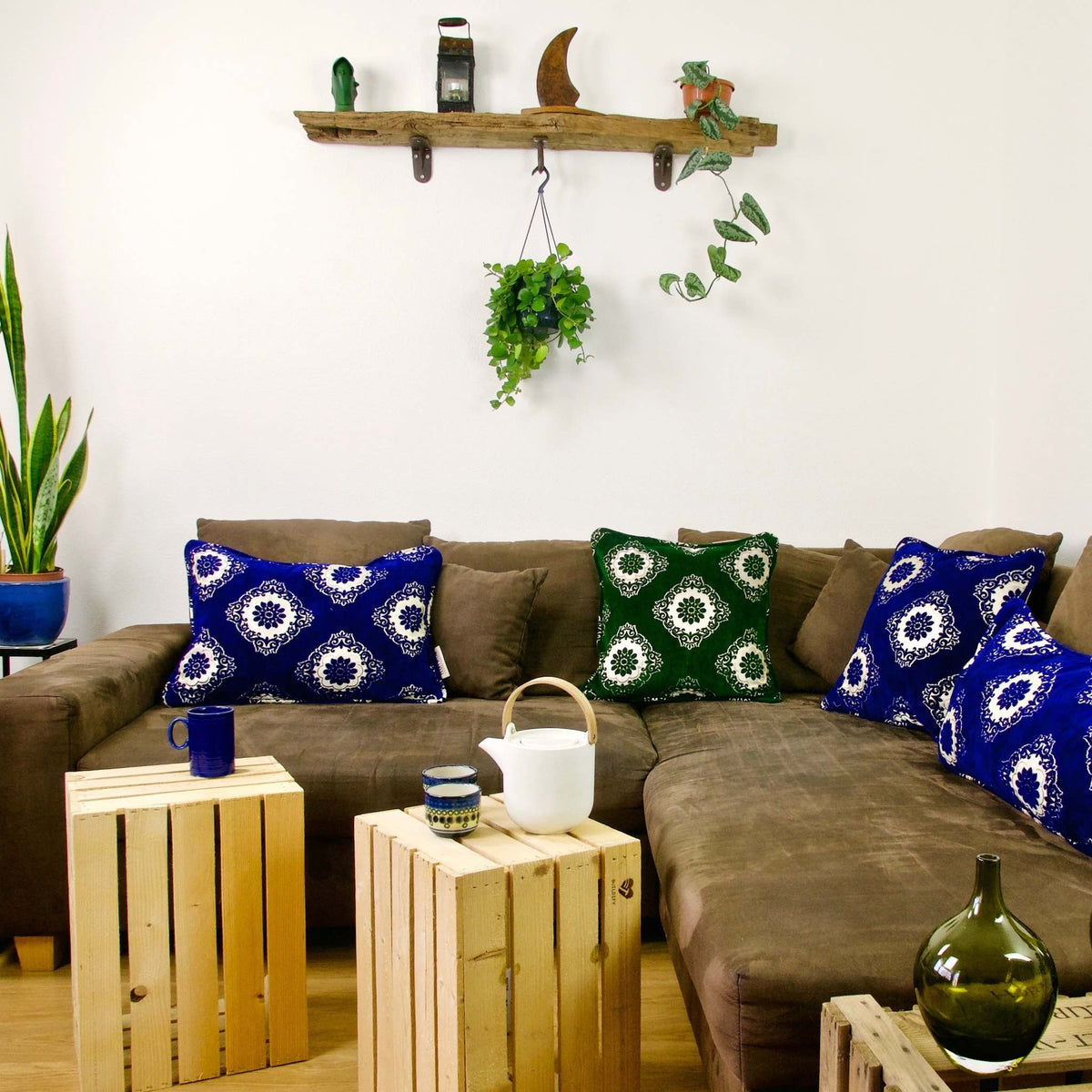 Three blue and one green velvet throw pillows on a couch.
